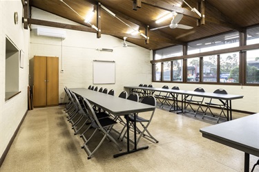 View of the dining hall with multiple tables and chairs setup accessible from the kitchen via a serving window