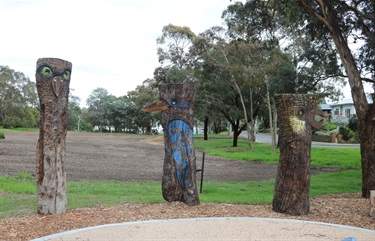 Multiple tree trunks raising up from the ground at various heights with artistic bird carvings cut out, detailed and painted