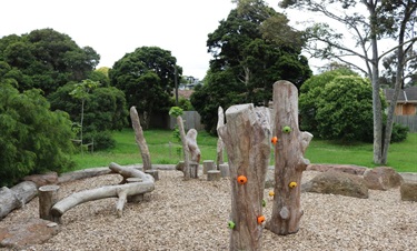 Repurposed tree trunks laying horizontally to create a balance beam, cut logs as steps and taller trunks raising up from the ground with moulded finger holds/grips for children to balance, step and climb as part of a nature play space.