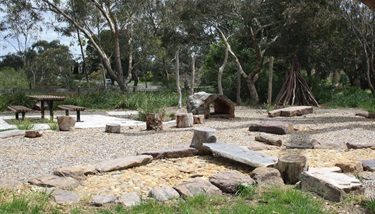 A playground in a local park, with repurposed tree trunks cut up to create steps for children to balance over as part of a nature play space.