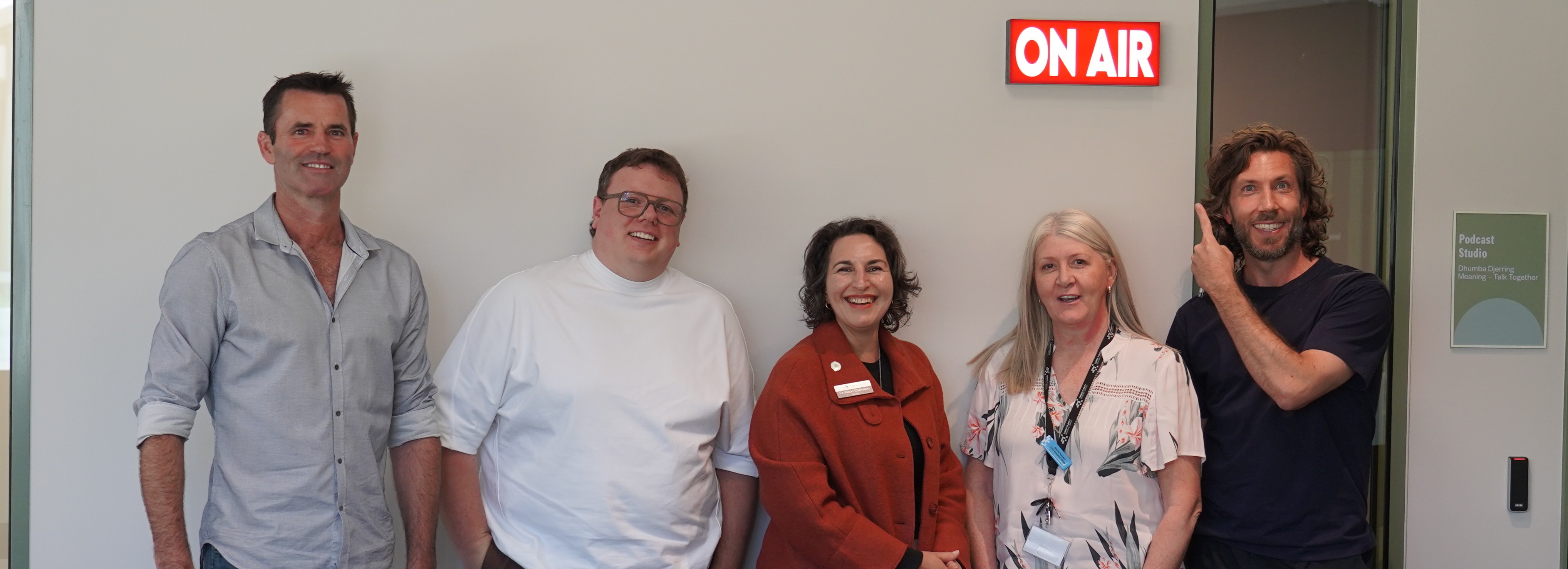 Group photo of the 5 people involved in the podcast recorded at Rosanna Library, with Shawn Neilsen pointing to the On Air sign out the front of the recording room